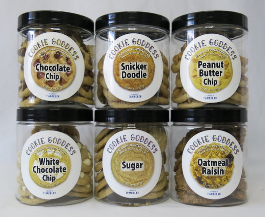 Six jars of 'Cookie Goddess' cookies with various flavors on a white background
