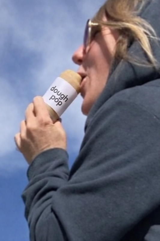 Person eating a dough pop against a blue sky